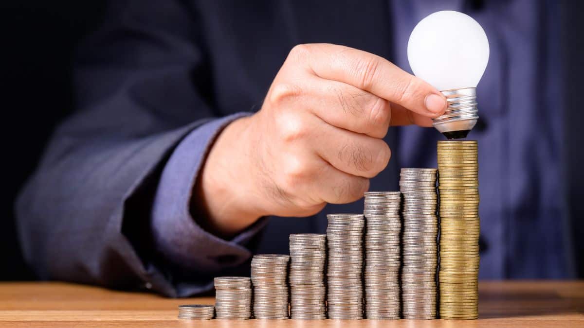 a hand holding a light bulb over a stack of coins